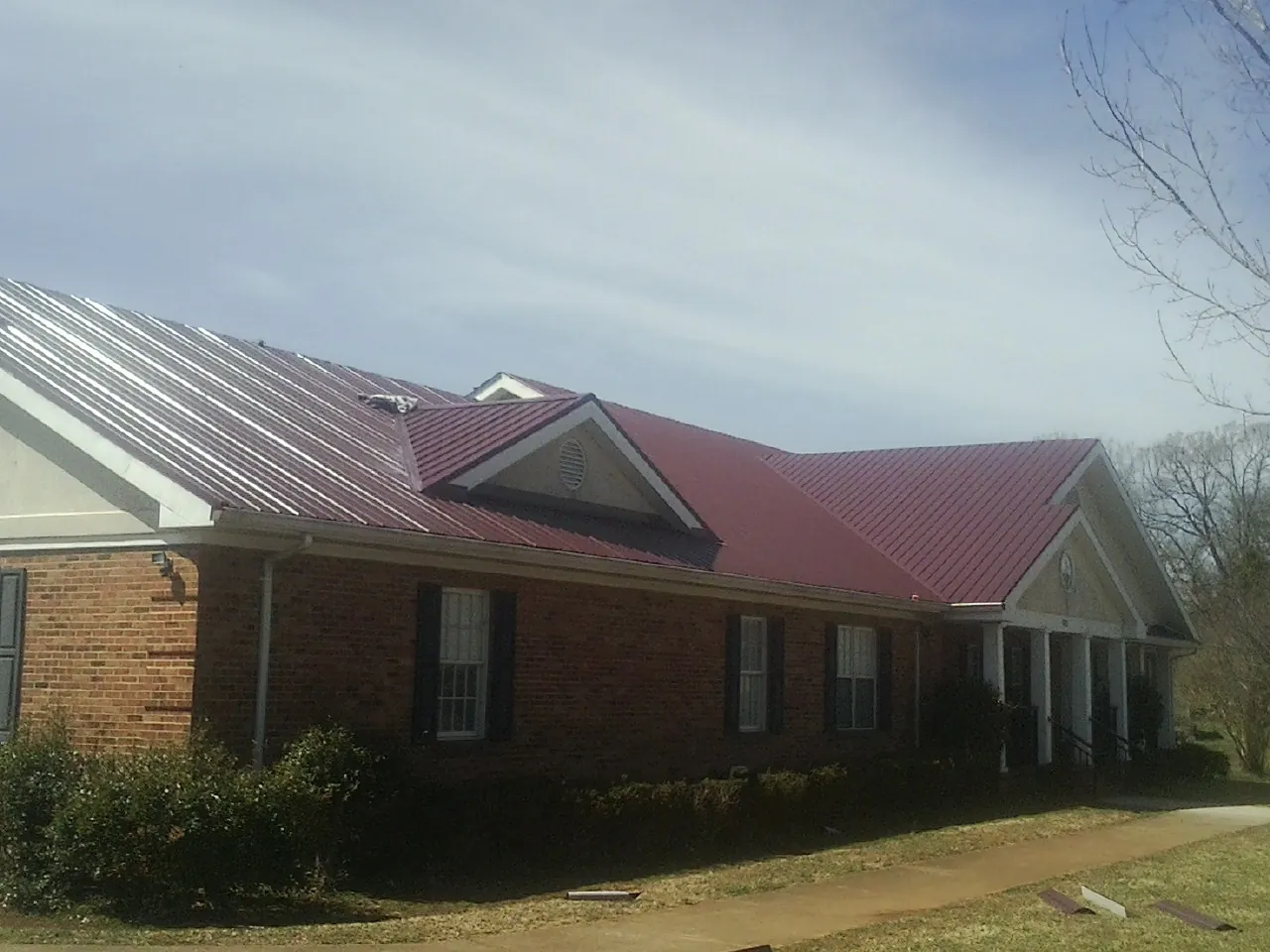 Red metal roof with gabled entries on a long brick building, from a Hail Damage Roof Repair job in Essington