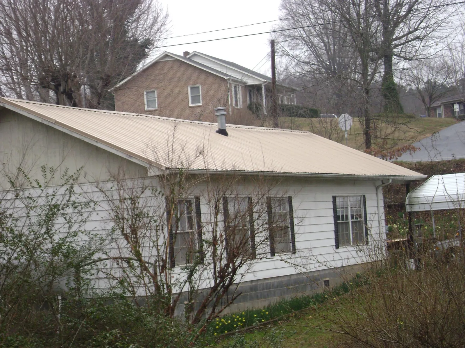 Tan metal roof on a white sided house set into a hillside — Commercial Roofing by Roofing Brothers in Essington